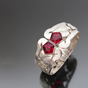 May include: A silver bracelet with two red gemstones and a grapevine design.