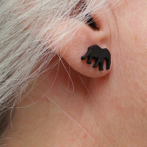 Könnte beinhalten: Ein Paar schwarze Elefanten-Silhouetten-Ohrstecker. Die Ohrringe sind klein und zart und eine großartige Möglichkeit, jedem Outfit einen Hauch von Verspieltheit zu verleihen.