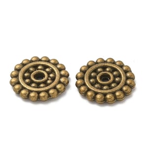 以下が含まれることがあります： 中央に穴が開いた、隆起した円形のデザインが施された、アンティークゴールド調の金属製の丸いビーズが2つです。