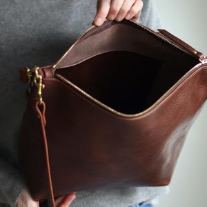 Puede incluir: Un bolso tote de cuero marr&oacute;n con cremallera dorada y una correa larga. El bolso est&aacute; abierto y el interior est&aacute; forrado con tela marr&oacute;n.