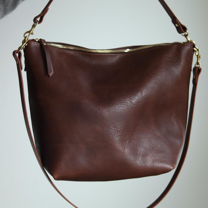 Puede incluir: Un bolso de hombro de cuero marr&oacute;n con una cremallera dorada y una correa larga ajustable.