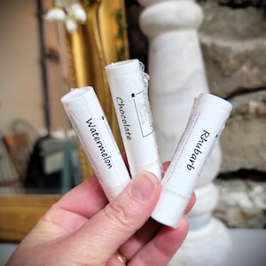 May include: Three white lip balm tubes with different scents: Rhubarb, Chocolate, and Watermelon. The tubes are labelled with the scent name and "Crafty Chicks Studios".