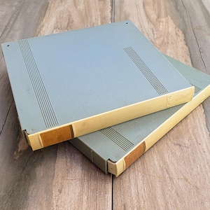 May include: Two gray and beige vintage audio cassette tapes stacked on top of each other. The tapes have a textured surface and a beige trim.