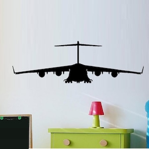 May include: Black silhouette of a C-17 Globemaster III cargo plane on a white wall. The plane is facing forward with its wings spread out.