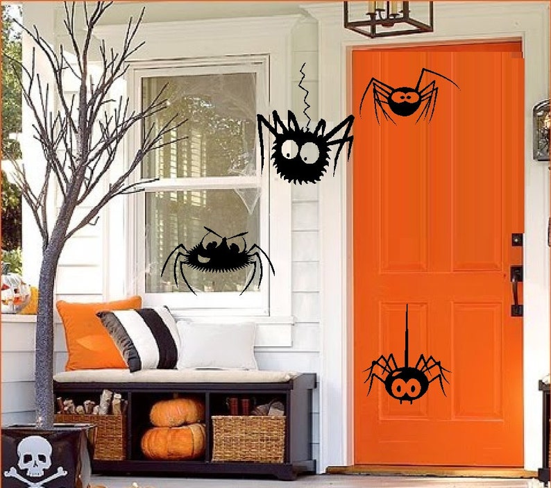 May include: A white door with a bright orange door, decorated with black spider cutouts. The door is surrounded by a white trim and a white wall. There is a window to the left of the door with a black spider cutout on the glass.