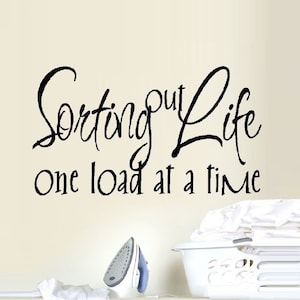May include: A black and white wall decal with the text "Sorting out life one load at a time". The decal is placed above a white laundry basket and an iron.