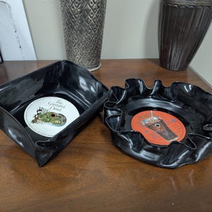 May include: Two black, upcycled vinyl record bowls. One is square, the other is round with a ruffled edge. The square bowl contains a record with the text "The Grateful Dead". The round bowl contains a record with an orange label.