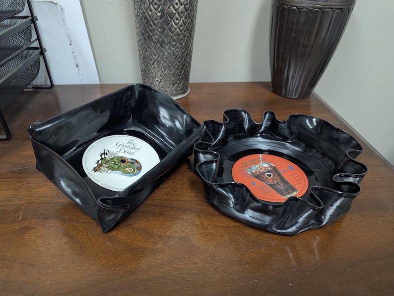 May include: Two black, upcycled vinyl record bowls. One is square, the other is round with a ruffled edge. The square bowl contains a record with the text "The Grateful Dead". The round bowl contains a record with an orange label.