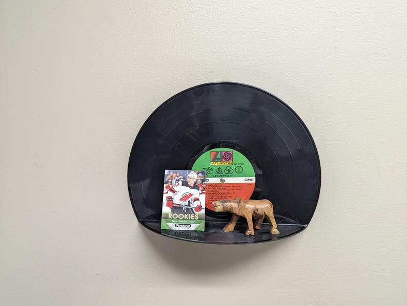 May include: A black vinyl record shelf with a hockey card and a wooden animal figurine. The hockey card features the word "ROOKIES" and images of hockey players. The figurine is a light brown color.