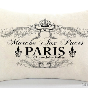 K&ouml;nnte beinhalten: Ein wei&szlig;es Kissen mit schwarzem Text und einem dekorativen Design. Der Text lautet "Marche Aux Puces Paris No. 07, rue Jules Vall&eacute;s".