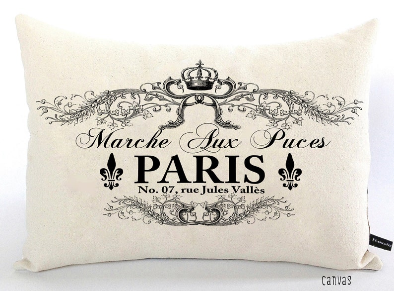 K&ouml;nnte beinhalten: Ein wei&szlig;es Kissen mit schwarzem Text und einem dekorativen Design. Der Text lautet "Marche Aux Puces Paris No. 07, rue Jules Vall&eacute;s".
