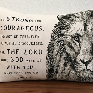 May include: A white throw pillow with black text and a black and white illustration of a lion's face. The text reads "Be strong and courageous. Do not be terrified: Do not be discouraged, for the Lord your God will be with you wherever you go. Joshua 1:9."