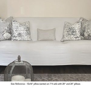 K&ouml;nnte beinhalten: Ein wei&szlig;es Sofa mit einem wei&szlig;en &Uuml;berwurf und drei Kissen. Das mittlere Kissen ist ein 30,5 x 40,6 cm gro&szlig;es Leinenkissen. Die beiden seitlichen Kissen sind 50,8 cm und 61 cm gro&szlig; und haben einen schwarz-wei&szlig;en Blumendruck mit franz&ouml;sischem Text. Das Sofa steht auf einem gemusterten Teppich.