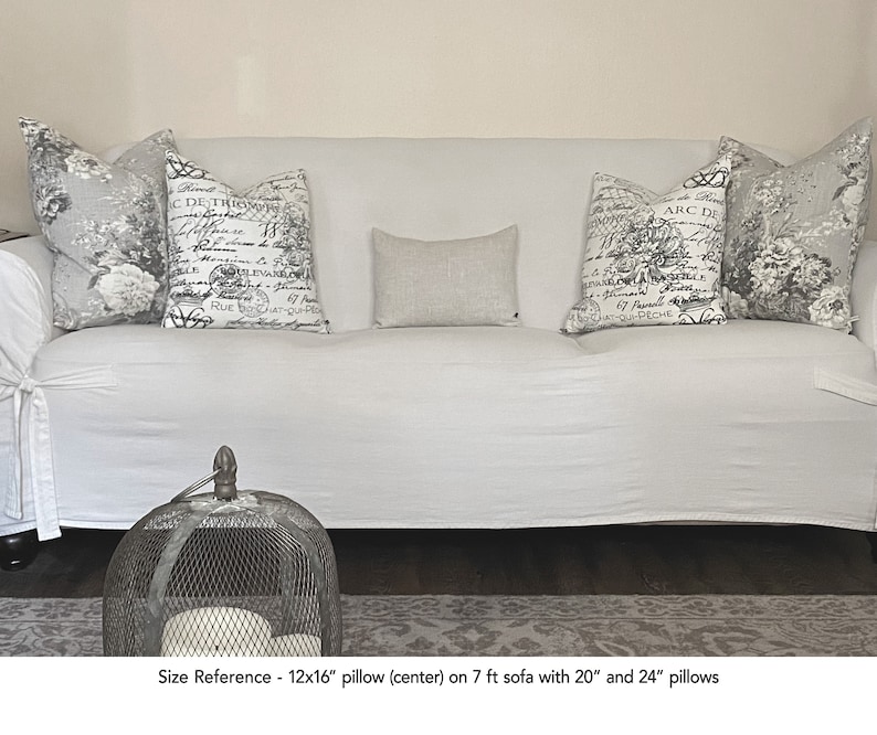 K&ouml;nnte beinhalten: Ein wei&szlig;es Sofa mit einem wei&szlig;en &Uuml;berwurf und drei Kissen. Das mittlere Kissen ist ein 30,5 x 40,6 cm gro&szlig;es Leinenkissen. Die beiden seitlichen Kissen sind 50,8 cm und 61 cm gro&szlig; und haben einen schwarz-wei&szlig;en Blumendruck mit franz&ouml;sischem Text. Das Sofa steht auf einem gemusterten Teppich.