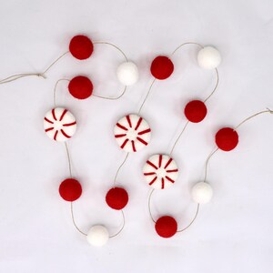 May include: A festive garland featuring red and white felt balls and peppermint-shaped ornaments. The garland is strung on natural twine, ideal for holiday decor. The red balls and peppermint shapes are approximately 2.5 cm in diameter.