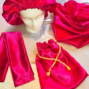 May include: A set of pink satin hair accessories including a bonnet, a scrunchie, and a drawstring bag. The bag has a gold drawstring.