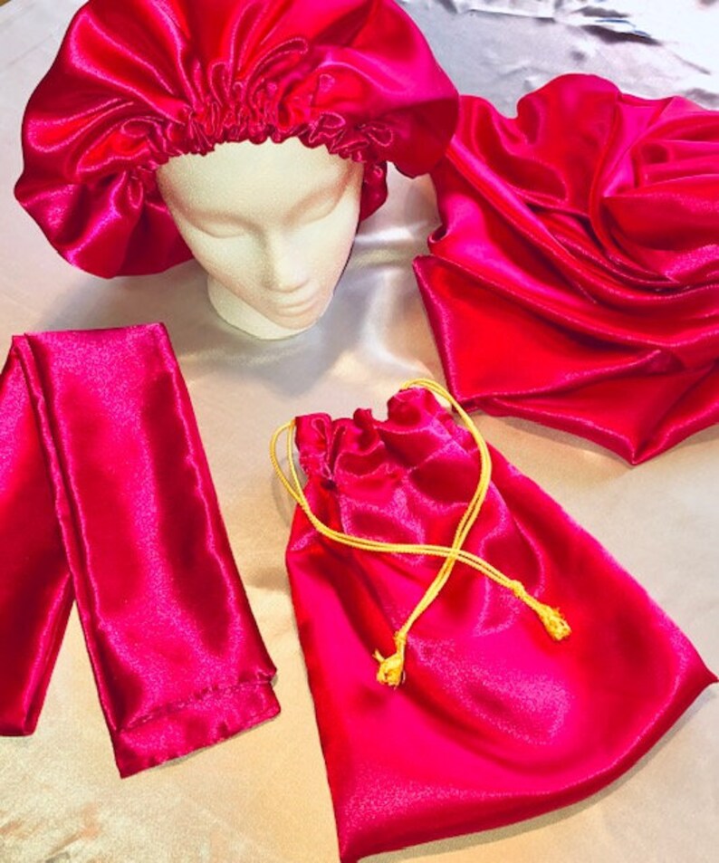 May include: A set of pink satin hair accessories including a bonnet, a scrunchie, and a drawstring bag. The bag has a gold drawstring.