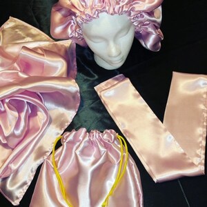 May include: A set of pink satin hair accessories including a bonnet, a scarf, and a drawstring bag. The bag has yellow drawstrings.