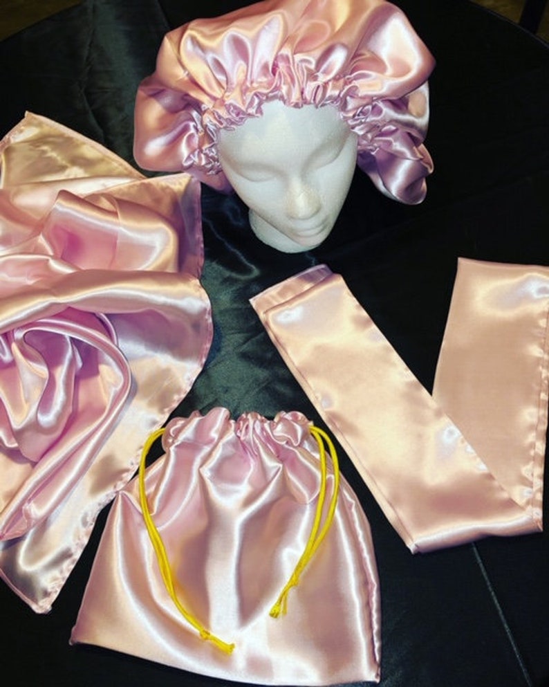 May include: A set of pink satin hair accessories including a bonnet, a scarf, and a drawstring bag. The bag has yellow drawstrings.