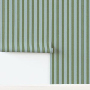 May include: A roll of wallpaper featuring a vertical striped pattern with alternating bands of light blue and olive green. The stripes have a textured, hand-painted appearance with thin, darker green lines running through the center of each olive band.