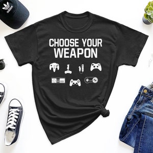 May include: Black t-shirt with the text "Choose Your Weapon" and a variety of video game controller icons in white.