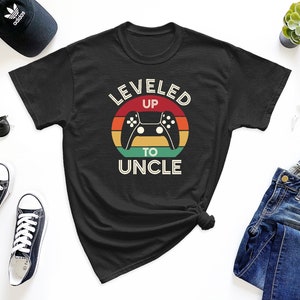 May include: Black t-shirt with a retro-style graphic that says "Leveled Up To Uncle" with a video game controller in the center.