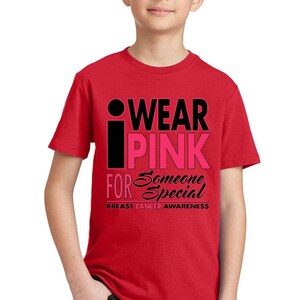 May include: Red t-shirt with a black and pink graphic that says "I Wear Pink For Someone Special" and "Breast Cancer Awareness".
