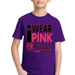 May include: Purple t-shirt with a black and pink graphic that says "I Wear Pink For Someone Special" and "Breast Cancer Awareness".