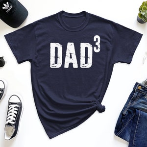 May include: A navy blue t-shirt with the text "DAD³" in white distressed lettering.