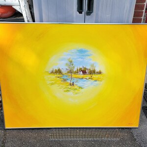 May include: A framed landscape painting with a bright yellow background. The painting features a central scene of a house, trees, and a river under a blue sky. The artwork is enclosed in a silver frame.