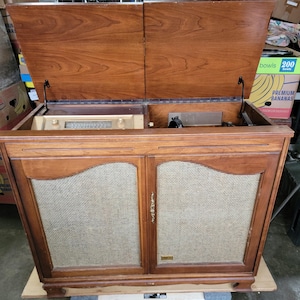 May include: A vintage wooden stereo console with a record player and radio. The top lid is open, revealing the turntable and radio controls. The console has two doors with speaker grilles.