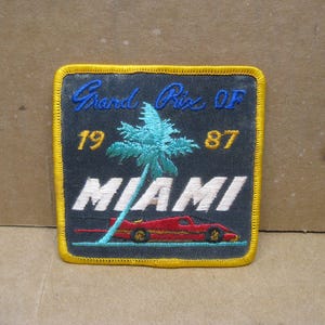 May include: A blue and yellow embroidered patch with the text "Grand Prix of 1987 Miami" and a palm tree and a red race car.