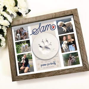 May include: A rectangular wooden frame containing a collage of five photographs of a white dog, a central circular clay mold with a 4-inch paw print, and the text Sam, 2005-2020, and You left paw prints on our hearts in blue and black lettering.