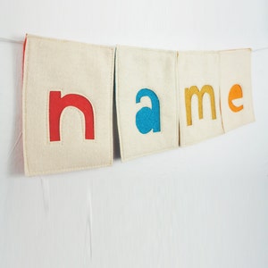 May include: A felt banner with the word "name" spelled out in colorful letters. The letters are red, blue, yellow, and orange.