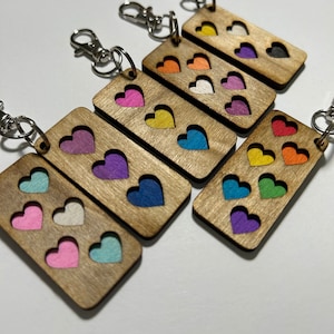 May include: Set of six wooden keyrings with different coloured hearts. Each keyring has three hearts in different colours, including pink, blue, purple, yellow, orange and green.
