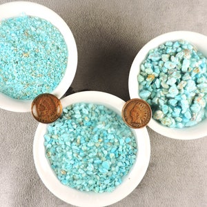 May include: Three white bowls filled with turquoise stones of varying sizes. The bowls are arranged in a triangular shape with a copper coin in between each bowl.