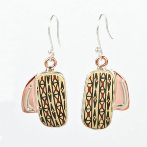 Peut inclure: Une paire de boucles d'oreilles pendantes en argent avec un motif géométrique en noir, rouge et or sur fond crème. Les boucles d'oreilles ont un accent en cuivre.