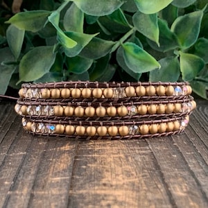 May include: A brown leather wrap bracelet with gold beads and clear crystal beads.