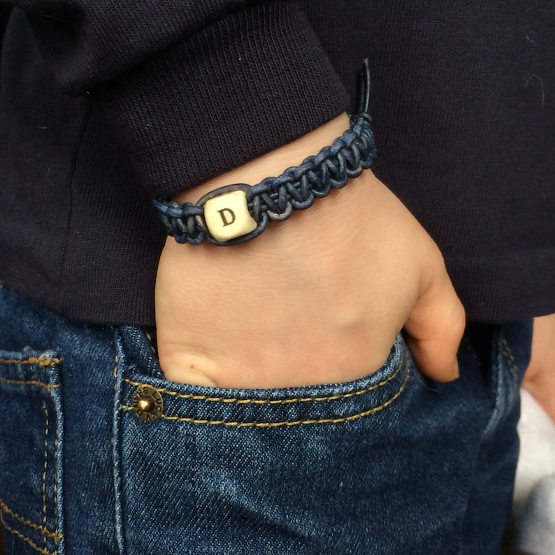 K&ouml;nnte beinhalten: Ein blaues geflochtenes Armband mit einem goldenen Anh&auml;nger, auf dem der Buchstabe 'D' eingraviert ist.