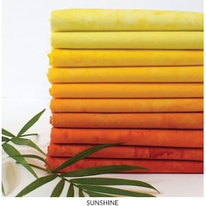 May include: A stack of fabric fat quarters in shades of yellow, orange, and red. The fabric is arranged in a gradient, transitioning from light yellow to deep orange. The text "SUNSHINE FAT QUARTER BUNDLE" is at the bottom.