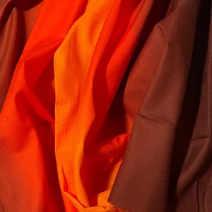 May include: An abstract image of layered fabric in shades of orange and brown. The colors transition from bright orange to a deep, rich brown, creating a sense of depth and texture. The folds and shadows add visual interest.