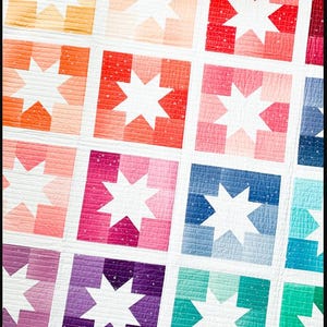 May include: A colorful quilt with a repeating pattern of white stars in squares with a gradient of colors. The quilt is made with a variety of fabrics, including pink, red, orange, yellow, green, blue, and purple.
