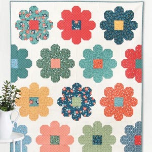 May include: A floral quilt with a white background and large, colorful flower designs. The flowers are in shades of red, blue, green, and orange, with patterned centers. The word "Daisy" is at the top.