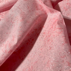 May include: Close-up of pink fabric with a marbled design. The fabric has a subtle shimmer and a textured appearance. The folds and shadows create depth and dimension, highlighting the fabric's soft texture.