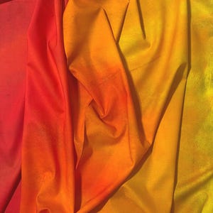 May include: A piece of fabric featuring a vibrant gradient that transitions from deep red on the left to bright yellow on the right. The material has a soft, folded texture. The selvage edge displays the text SKY by Jennifer Sampou Robert Kaufman.