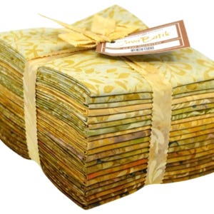 May include: A stack of folded fabric squares in shades of yellow, gold, and olive green with batik patterns. The fabric bundle is secured with a paper band and a tag that reads Java Batik 20 Fat Quarters, tied with a matching fabric ribbon.