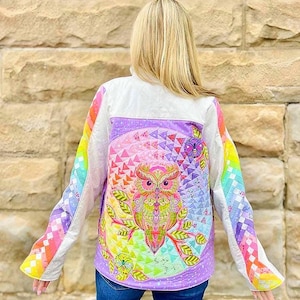 May include: A quilted jacket featuring a vibrant owl design. The jacket has a white body with rainbow-colored sleeves and a large owl illustration on the back. The owl is depicted in bright colors, with intricate details and geometric patterns.