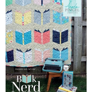 May include: A handmade quilt featuring a repeating pattern of open books in various colors. The quilt measures 54" x 66". A vintage teal typewriter, a teacup, and a stack of books are arranged in front of the quilt. The text "Book Nerd" is displayed.