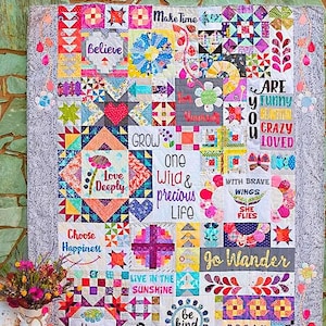 May include: A colorful patchwork quilt with various squares and patterns. The quilt features inspirational phrases like "Believe," "Love Deeply," and "Be Kind." The quilt is titled "Dear Daughter" by Sherri Noel. The quilt is displayed against a stone wall.