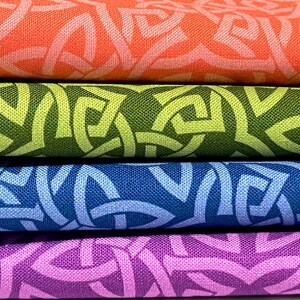 May include: A stack of four folded fabric pieces, each featuring a repeating geometric Celtic knot pattern. The colors from top to bottom are vibrant orange, olive green, deep blue, and bright purple, all with a visible woven texture.